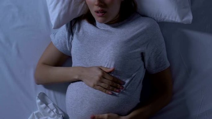 孕妇抱着肚子，躺在床上睡觉，姿势不舒服