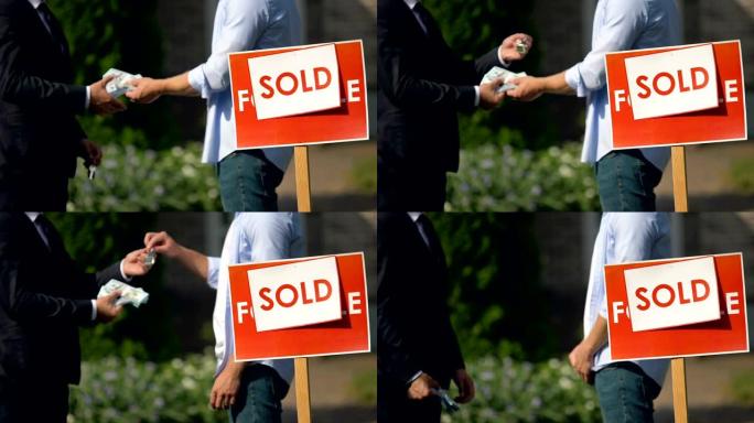 房地产经纪人和男子在出售的招牌上交换金钱和房屋钥匙