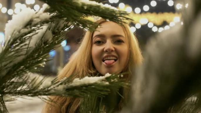 年轻女子躲在积雪覆盖的蓬松的树枝上。前景中雪中的圣诞树树枝