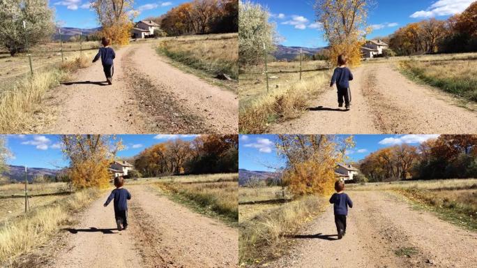 在晴朗的天空下，一个两岁的白人男孩沿着一条土路奔向西科罗拉多州的一所房子