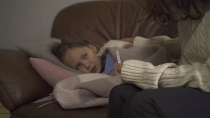生病的小女孩躺在家里的毯子下的特写镜头。悲伤的孩子有发热