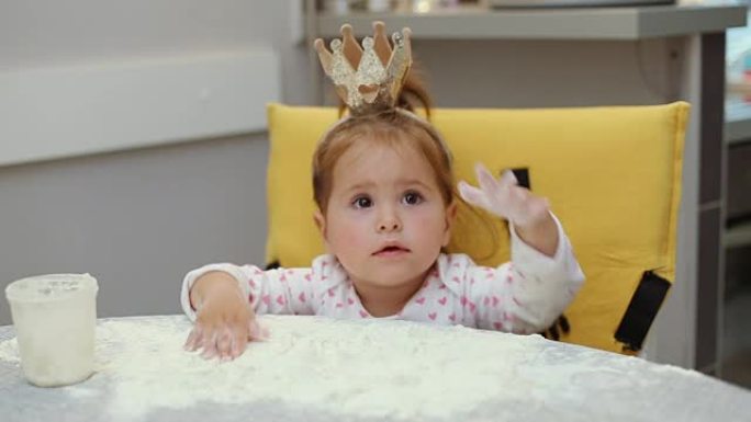 可爱的女婴在桌子上玩面粉，戴着皇冠