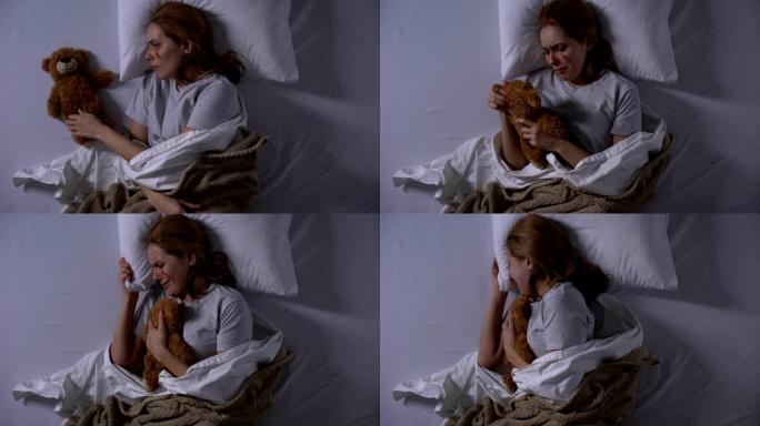 女性暴力受害者拥抱泰迪熊玩具，在床上哭泣，痛苦的情绪