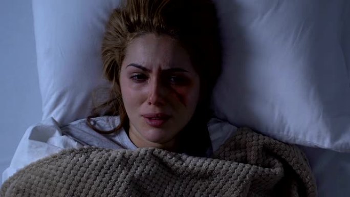 满脸伤痕的绝望女人躺在床上哭泣，性别暴力受害者