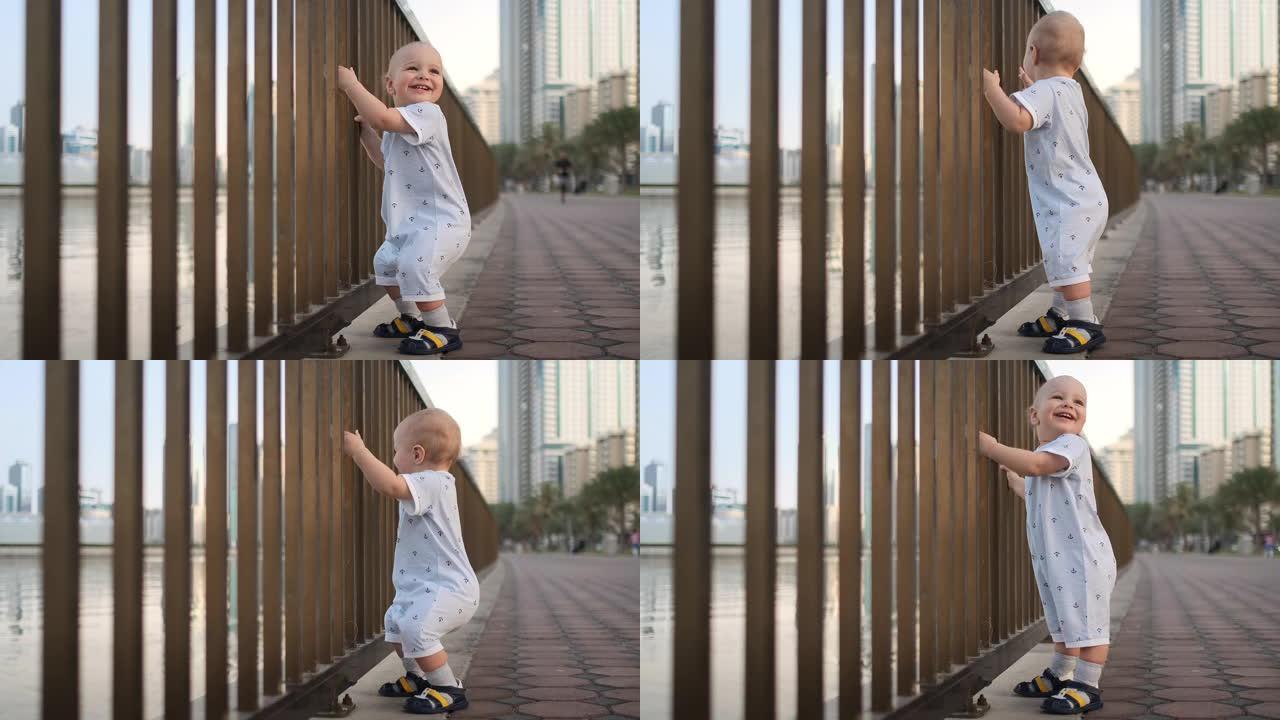 1岁那年的笑男孩，抱着栏杆跳舞，学习走路，迈出第一步，穿着白色连身裤站在海滨