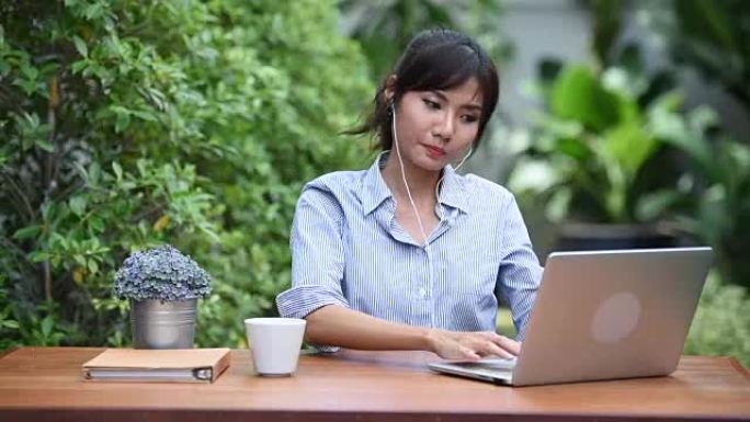 亚洲年轻女子在花园里使用笔记本网上购物