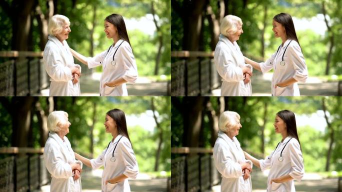 微笑的护士在sanatoria公园与穿着浴袍的老年妇女交谈，放松