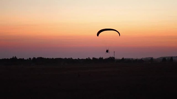 滑翔伞上的飞行员在日落之后用橙色在天空中飞行。背景