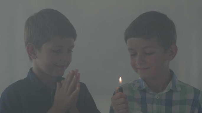 两个小兄弟在黑暗的烟雾弥漫的房间里玩打火机。
