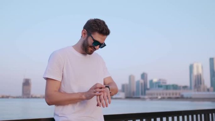 夏天站在海滨的一个年轻人使用智能手表屏幕