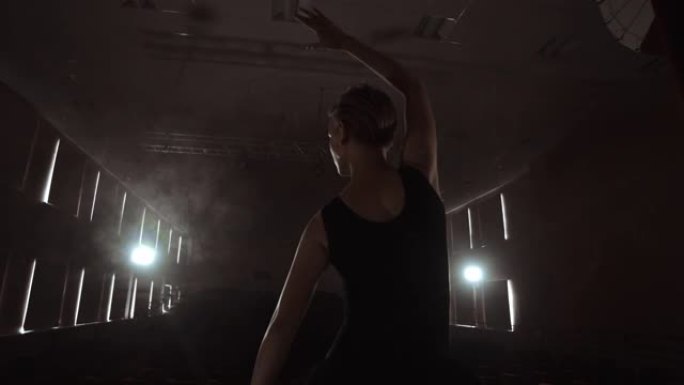 慢动作: 芭蕾舞女演员在黑暗的灯光下在舞台上的烟雾中穿着脚尖鞋跳舞。摄像机在万向节上移动。