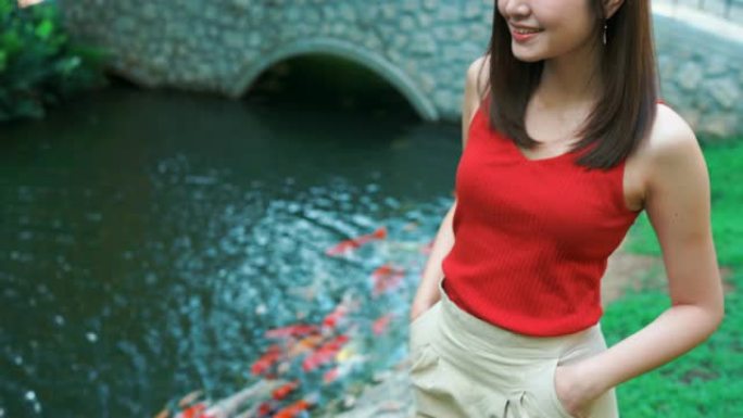 4k镜头美丽的年轻女子站在池塘边，用锦鲤鱼放松。