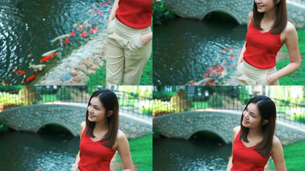 4k镜头美丽的年轻女子站在池塘边，用锦鲤鱼放松。
