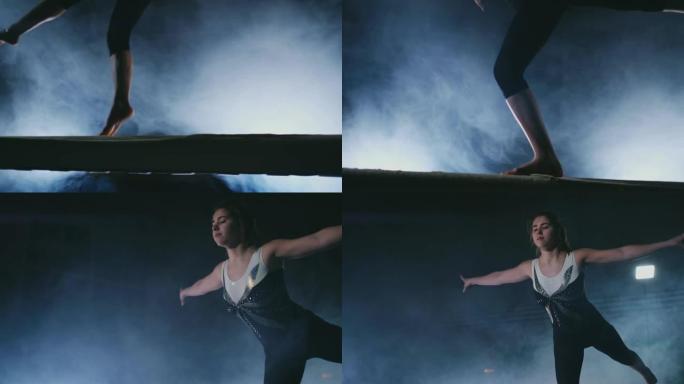 腿专业女孩体操运动员在平衡木上的烟雾中慢动作跳跃。女子艺术体操