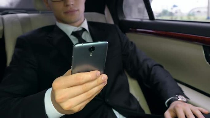 穿着西装的年轻人坐在汽车后座上使用智能手机，科技
