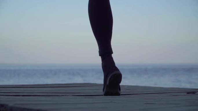 女性的双腿在户外的木制平台上跳舞。穿着紧身紧身裤和靴子的女人的腿在水面的背景下。