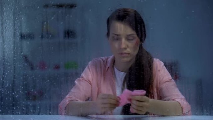 悲伤受伤的脸女士在雨天拿着粉红色的袜子，暴力后流产