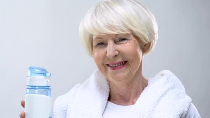 微笑的老妇人用毛巾和瓶装水，健康的生活方式，营养