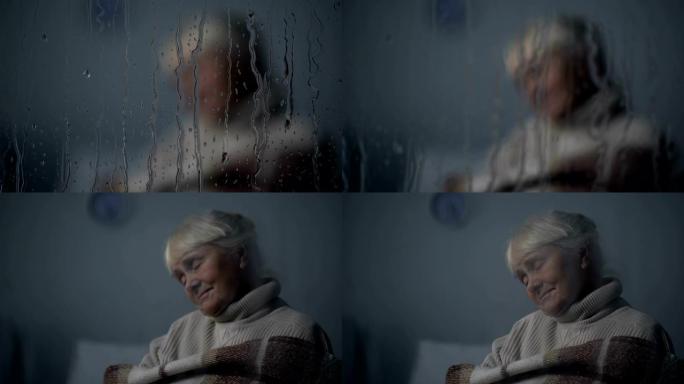可怜的老妇在养老院的雨天窗户后面的椅子上睡觉