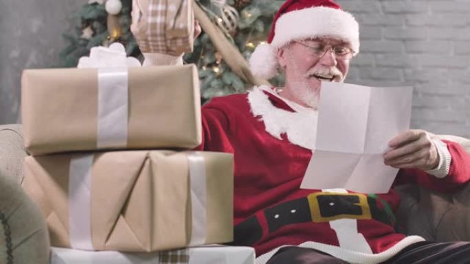 带有白胡子的圣诞老人的肖像读信，看着礼品盒，微笑着。戴眼镜的老人在除夕夜为孩子选择礼物。电影院4k 