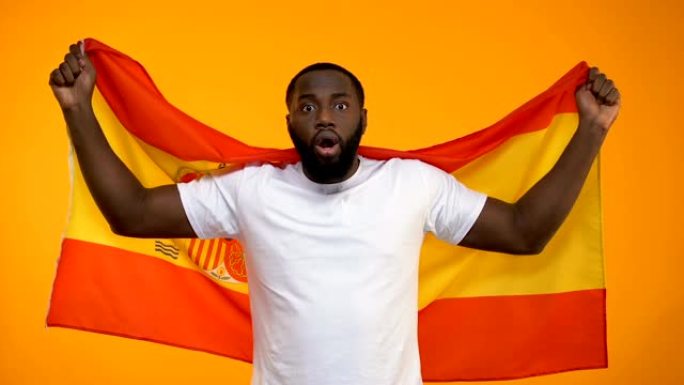 惊讶的非洲裔美国体育迷挥舞着西班牙国旗，为胜利欢呼
