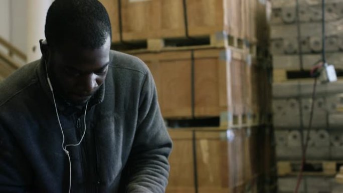 一个二十多岁的黑人留着胡须，在制造工厂用电钻旋转并拧紧黑色端盖