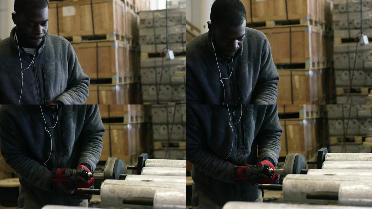 一个二十多岁的黑人留着胡须，在制造工厂用电钻旋转并拧紧黑色端盖