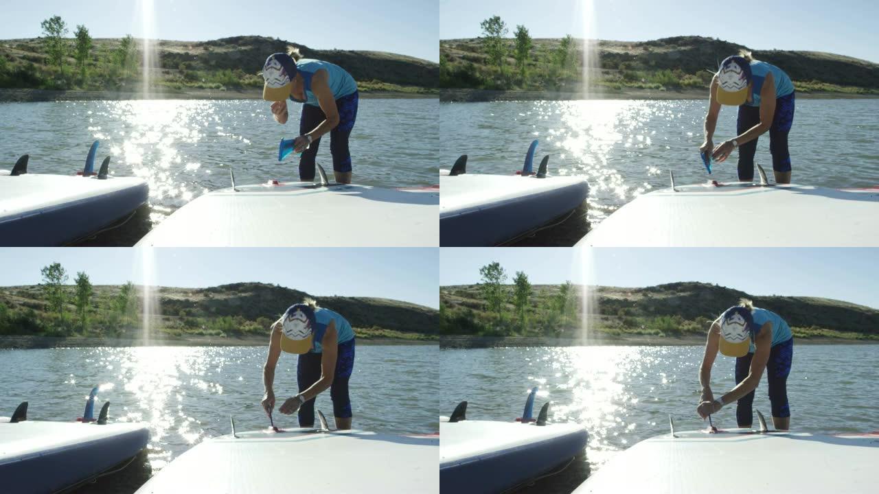 一名穿着运动服的白人妇女在科罗拉多州西部湛蓝的天空下，将鳍固定在桨板的底部，旁边是湖 (Snooks