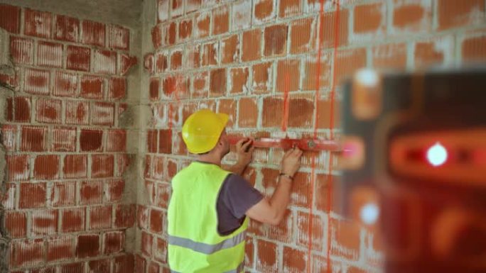 男性建筑工人在激光测量仪的帮助下在建筑物的墙壁上绘制水平线