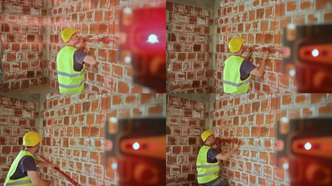 男性建筑工人在激光测量仪的帮助下在建筑物的墙壁上绘制水平线