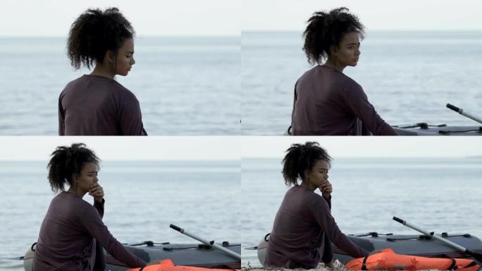 沮丧的女性难民坐在船附近的海岸上，逃离了祖国