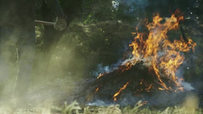 一名男子在户外用干草叉将木棍和树枝扔到一个大的燃烧燃烧堆上