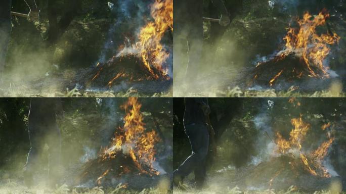 一名男子在户外用干草叉将木棍和树枝扔到一个大的燃烧燃烧堆上