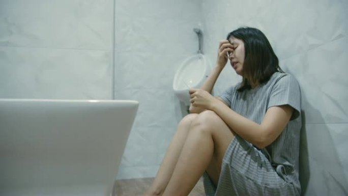 悲伤的女人坐在浴室的地板上，妊娠试验呈阴性