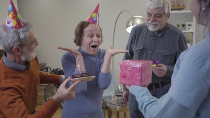 当志愿者和老人带来礼物和生日蛋糕时，激动的白人老妇睁开眼睛的肖像。在疗养院庆祝的女性退休人员。