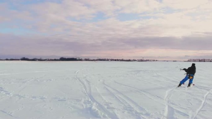 日落时，一个人在雪地里滑雪。他的降落伞拉了。风筝在雪地里冲浪