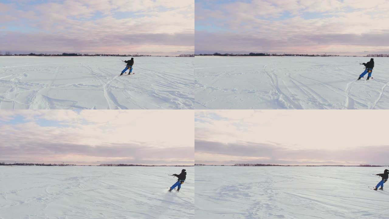 日落时，一个人在雪地里滑雪。他的降落伞拉了。风筝在雪地里冲浪