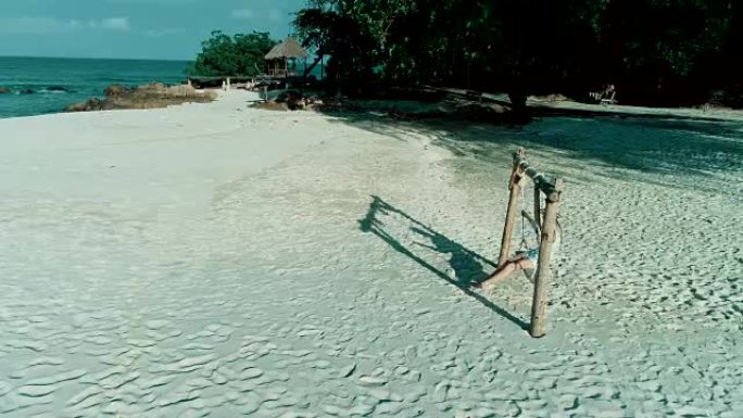 女人坐在沙滩上的秋千椅上，云雾的天空和漂亮的沙滩背景。