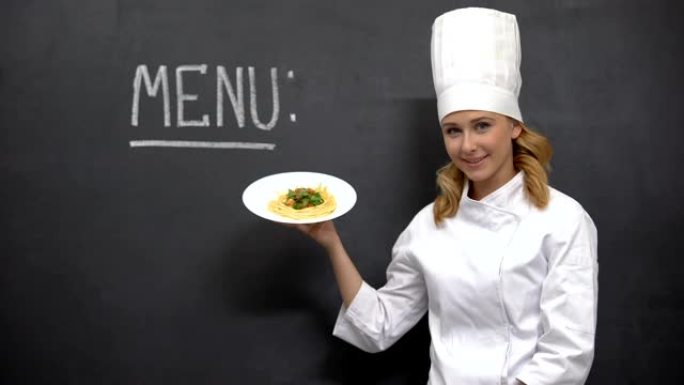 女厨师拿着面食盘，黑板上有菜单字，餐厅