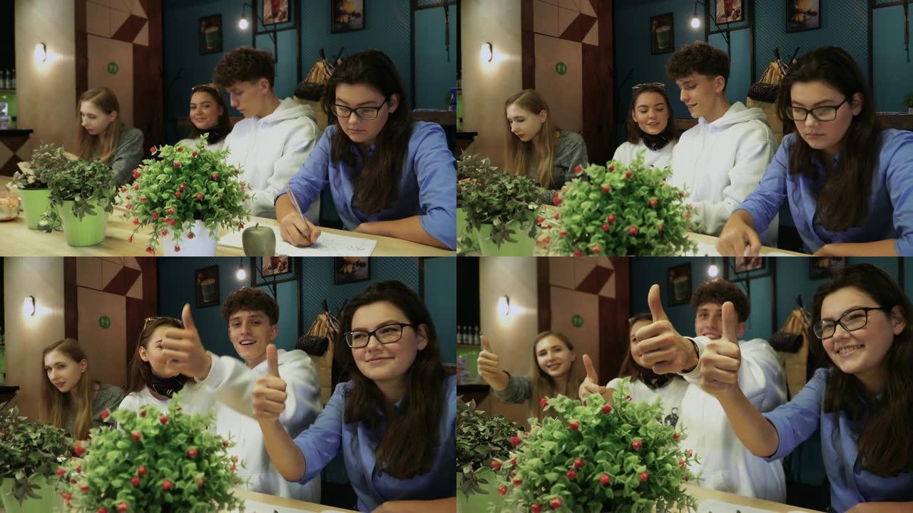四位同学坐在桌子旁做了一些事情，然后他们注意到自己被拍照了，他们开始微笑并举起了大手指