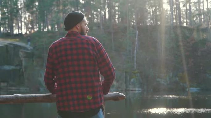 留着斧头的大胡子的人站在湖附近的森林里，欣赏着令人惊叹的景色。一个有斧头的人。