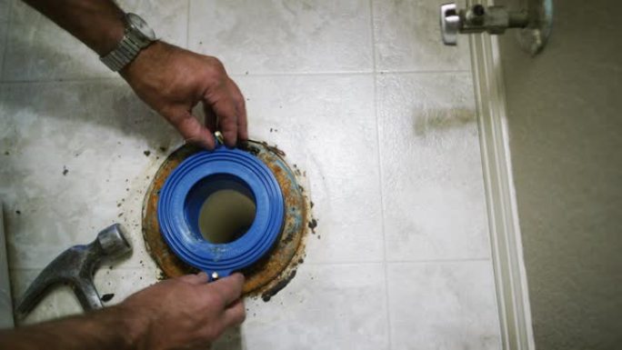 一名高加索杂工将橡胶垫圈放在法兰螺栓上，同时将破损的马桶固定在室内家用浴室中
