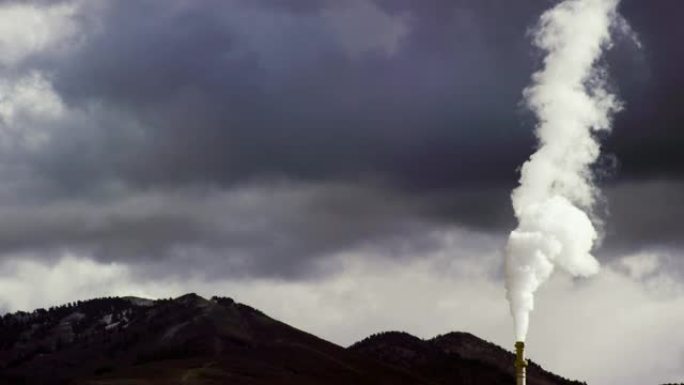 烟囱和烟雾来自一家炼油厂，背景是一座山，在戏剧性的多云天空下