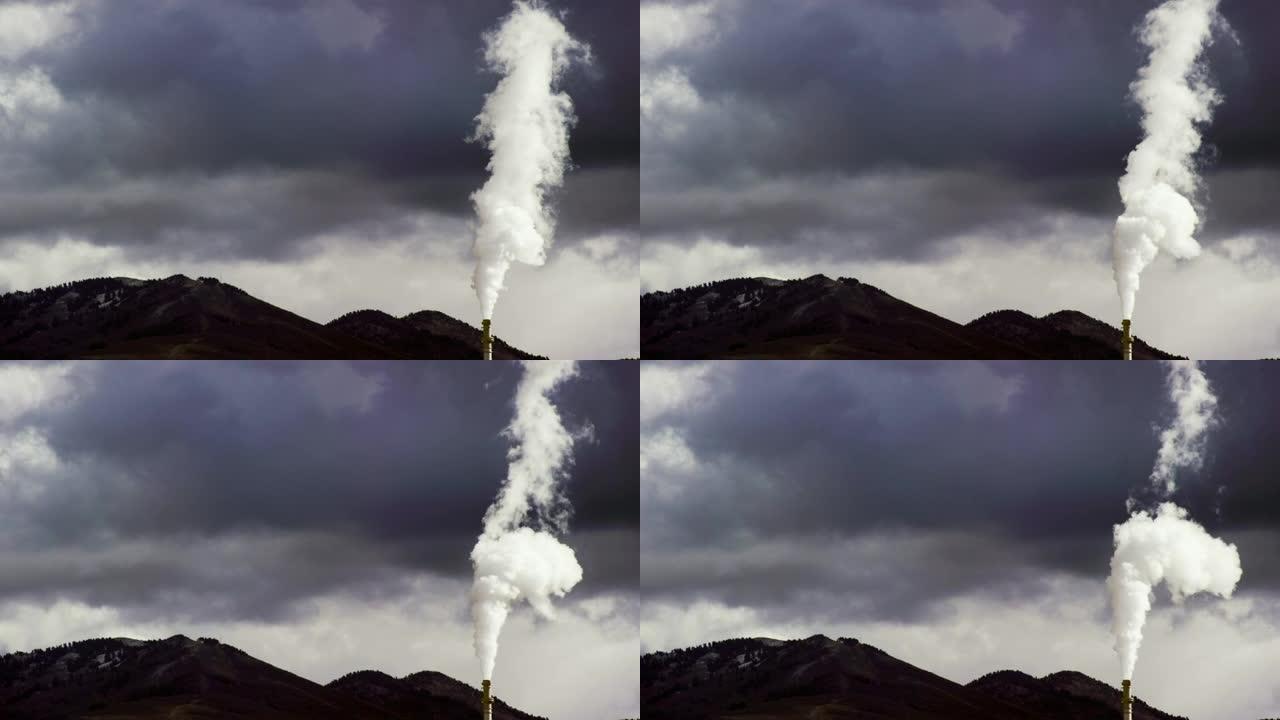 烟囱和烟雾来自一家炼油厂，背景是一座山，在戏剧性的多云天空下