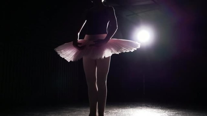 优雅的女孩在工作室练习芭蕾舞。黑色背景上聚光灯下芭蕾舞女演员的剪影。慢动作。
