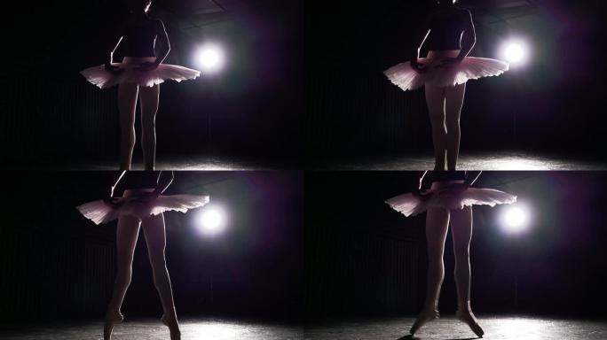 优雅的女孩在工作室练习芭蕾舞。黑色背景上聚光灯下芭蕾舞女演员的剪影。慢动作。