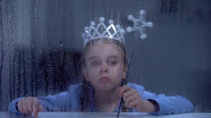 孤独的小公主戴着皇冠，魔术棒坐在下雨的窗户后面