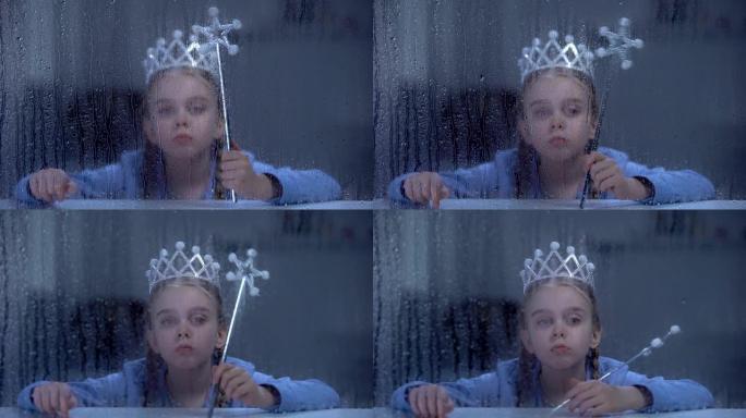 孤独的小公主戴着皇冠，魔术棒坐在下雨的窗户后面