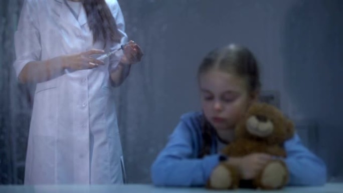 受惊的女孩抱着泰迪熊，背景上有注射器的护士，雨天
