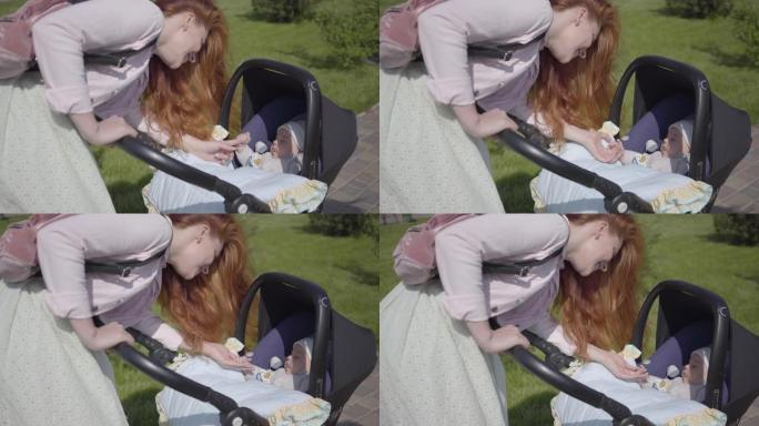 美丽的红发女人弯下腰在公园的婴儿车上。